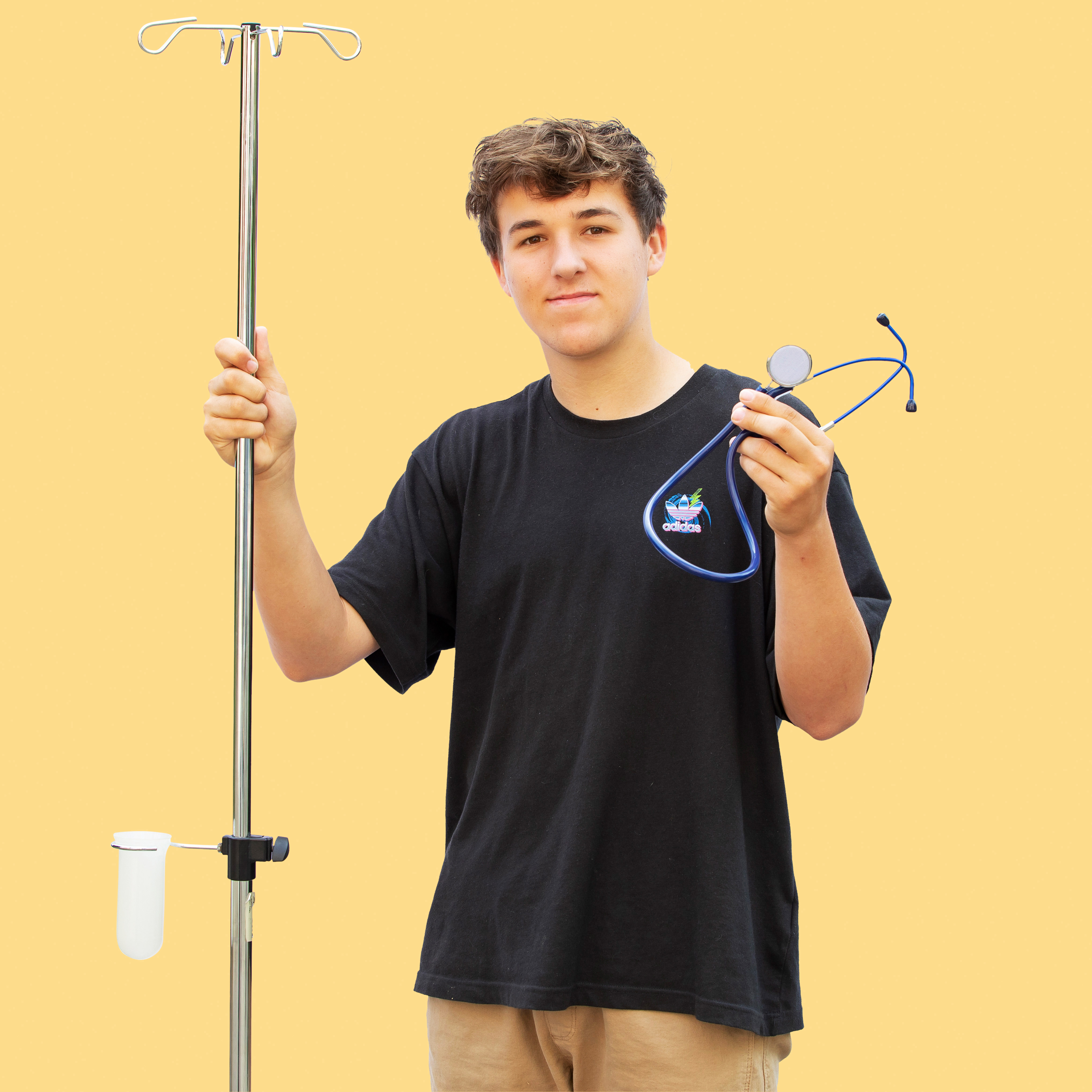 Jongen met een zwart shirt aan houdt een stethoscoop en een infuusstrandaard vast