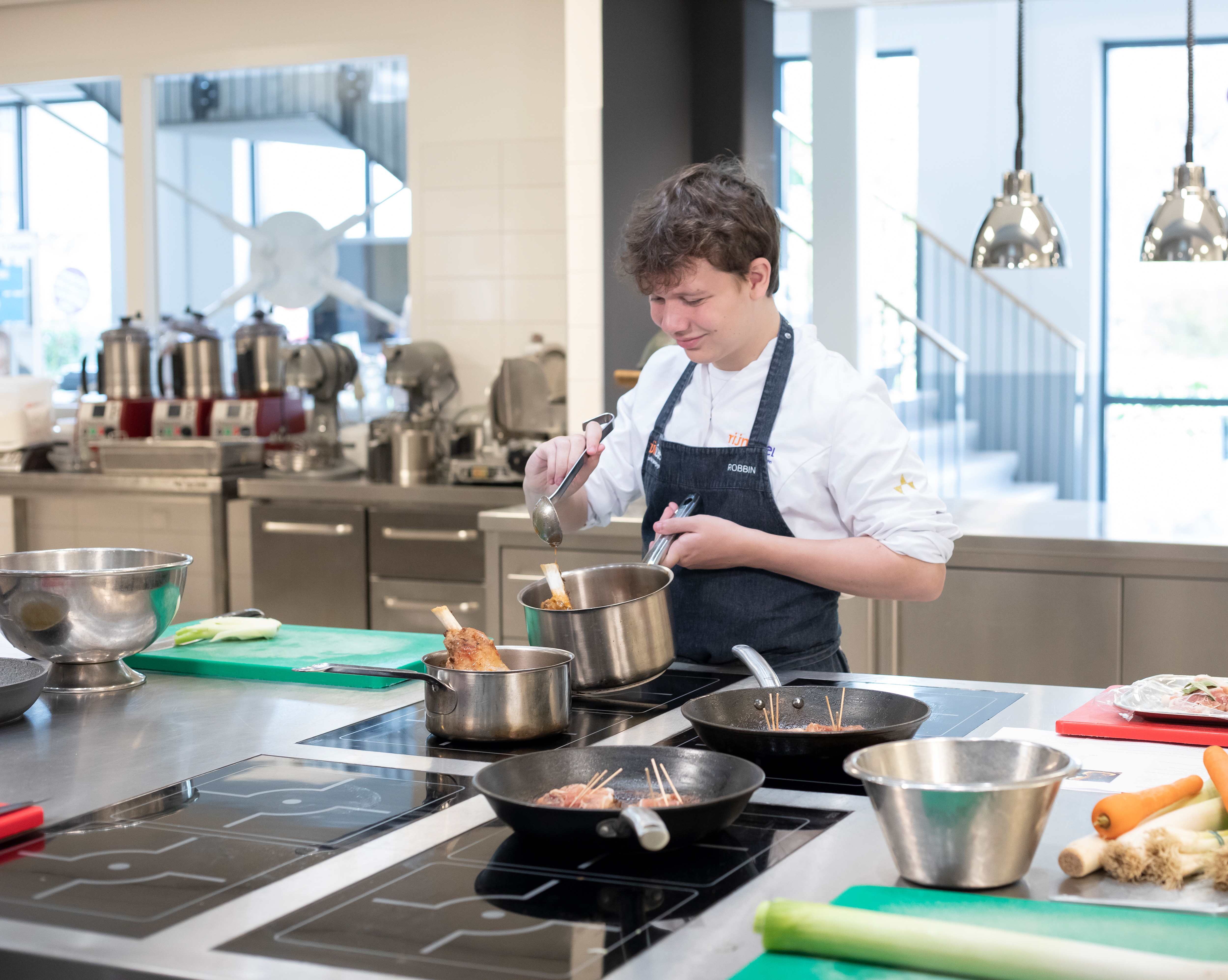 Jongen in kokskleding is aan het koken met een steelpan terwijl hij een lepel vasthoudt