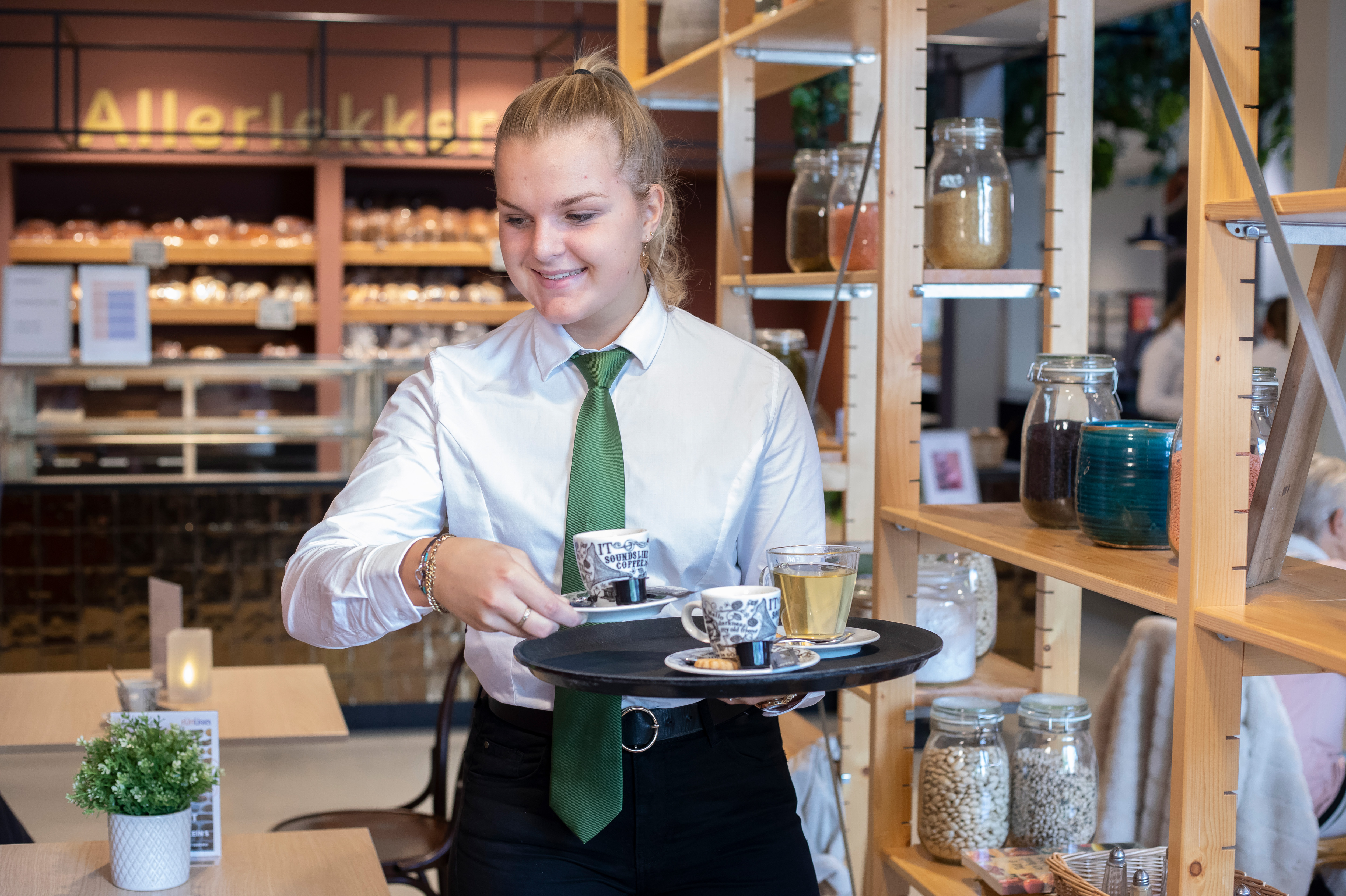 Meisje met een blouse en een stropdas loopt met een dienblad en brengt koffie en thee