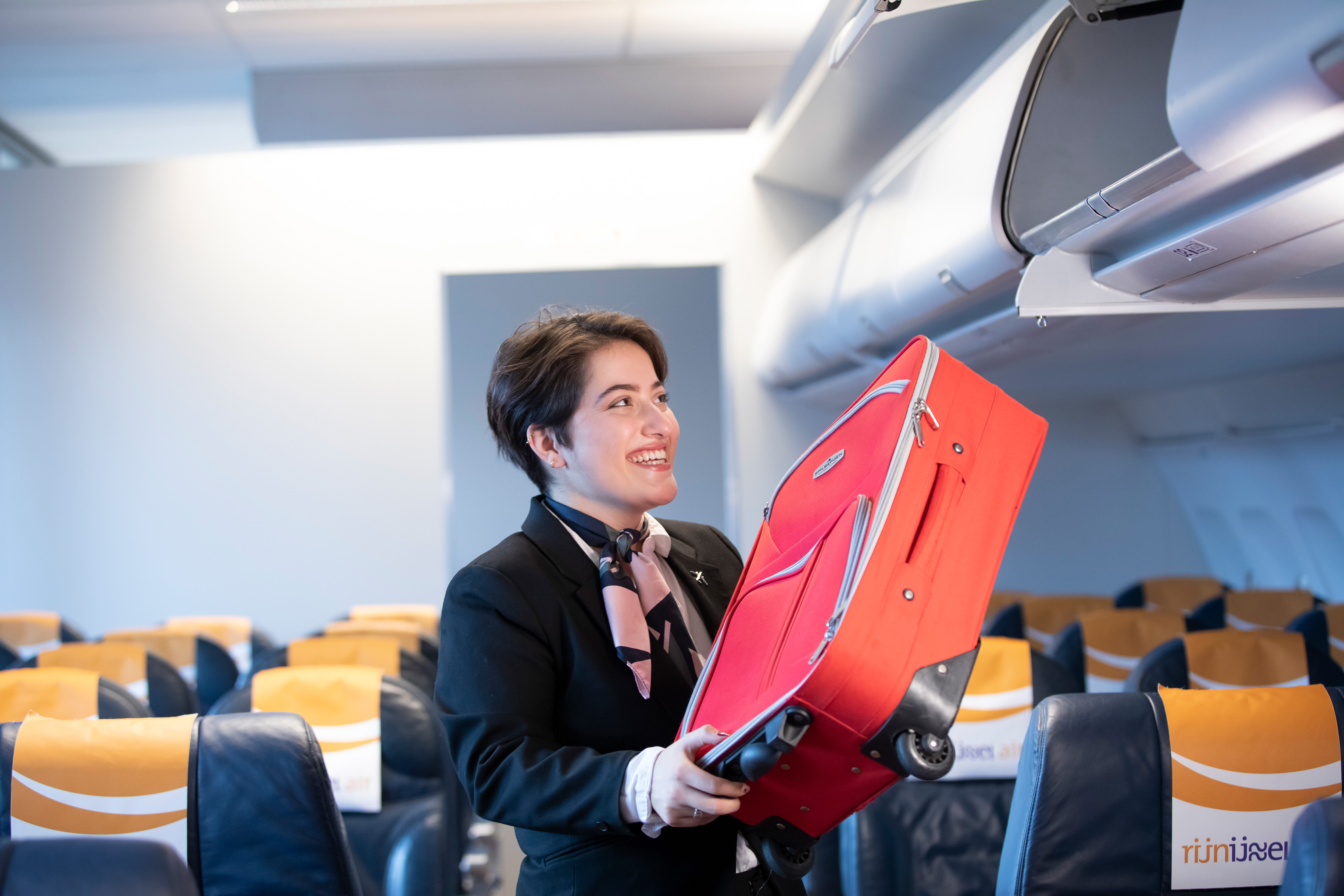 Student doet een koffer in het opbergbak van een vliegtuig