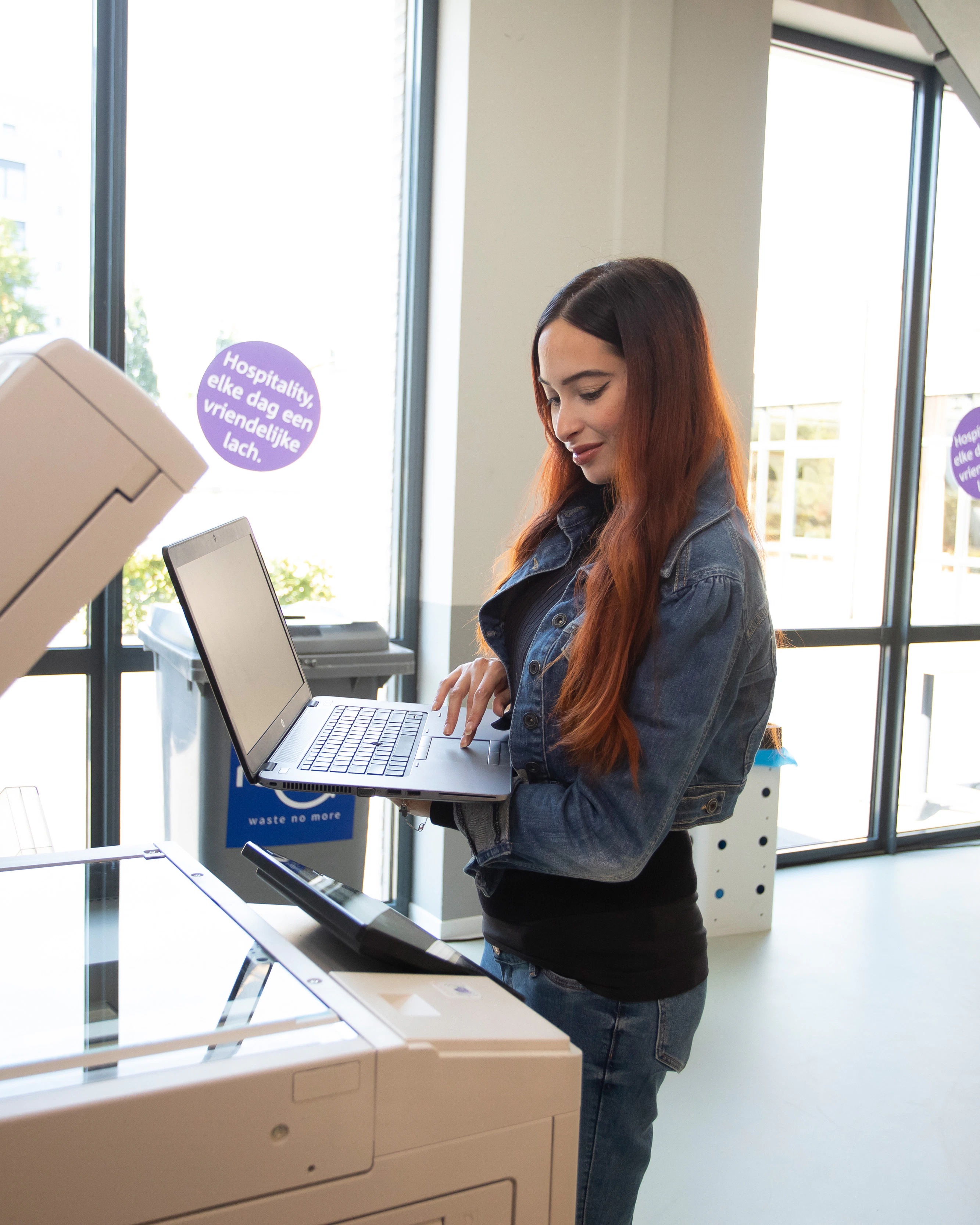 Een meisje staat met haar laptop achter de printer en scanner. Ze kijkt op haar laptop.