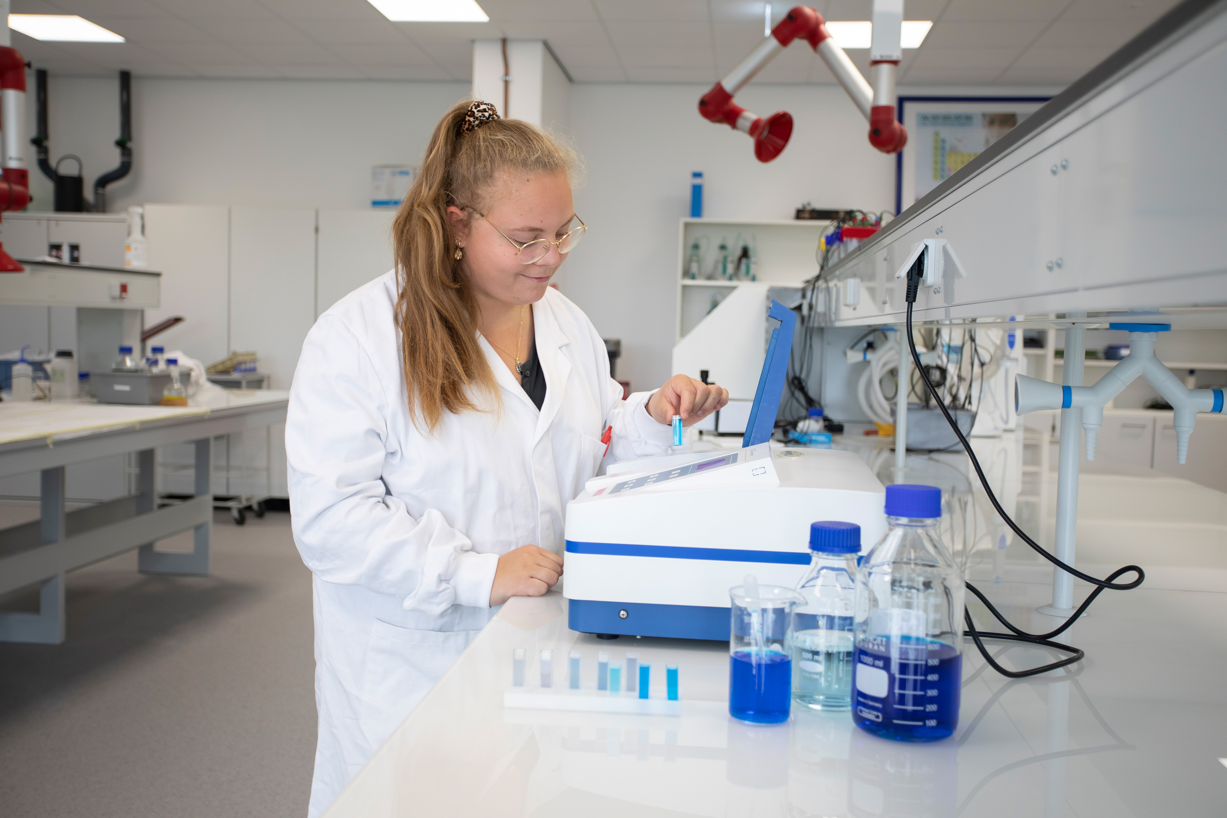 Meisje in een witte labaratoriumjas is bezig met blauwe chemische vloeistoffen in buisjes