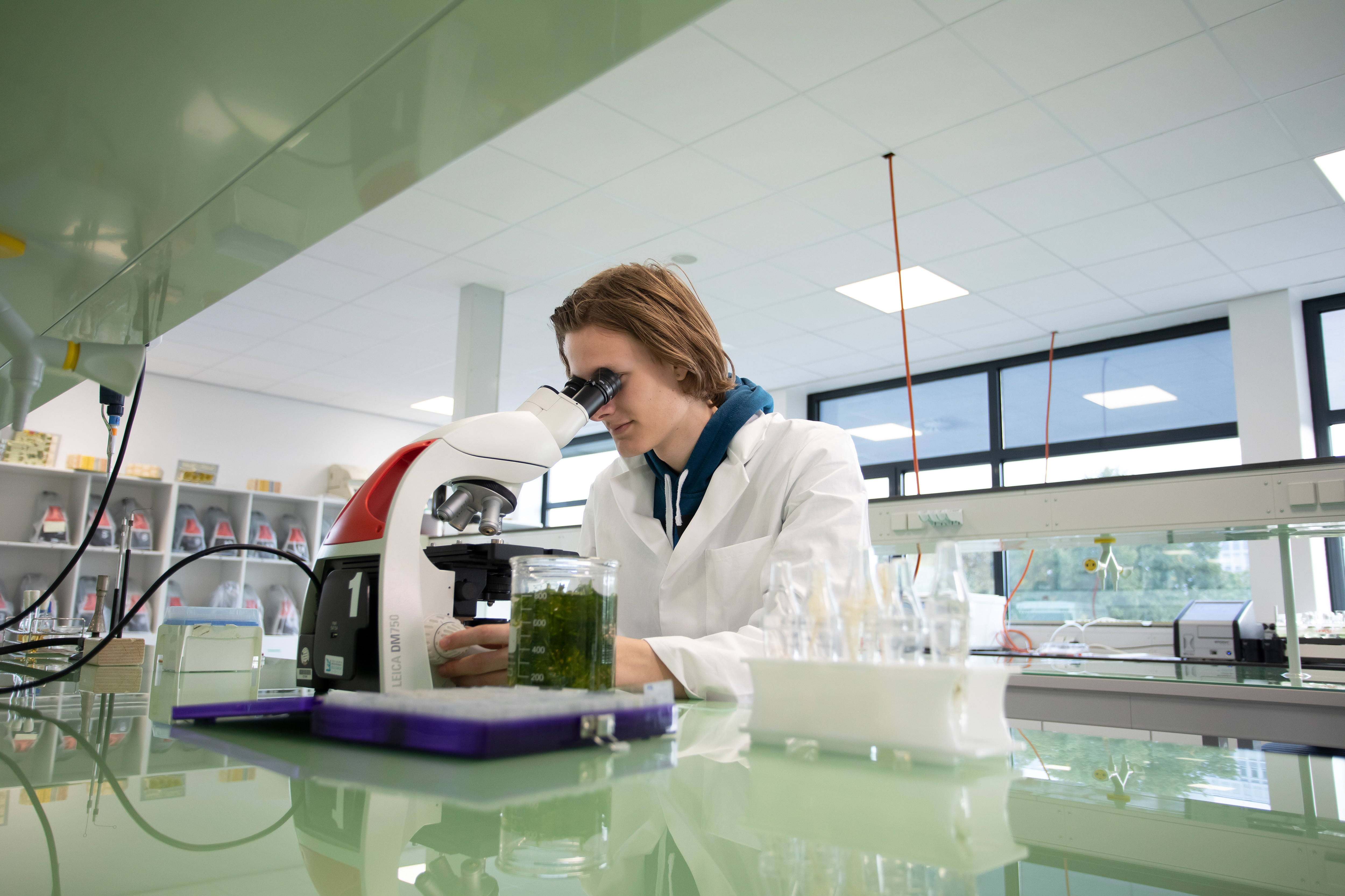 Jongen in een labaratoriumjas zit achter een microscoop