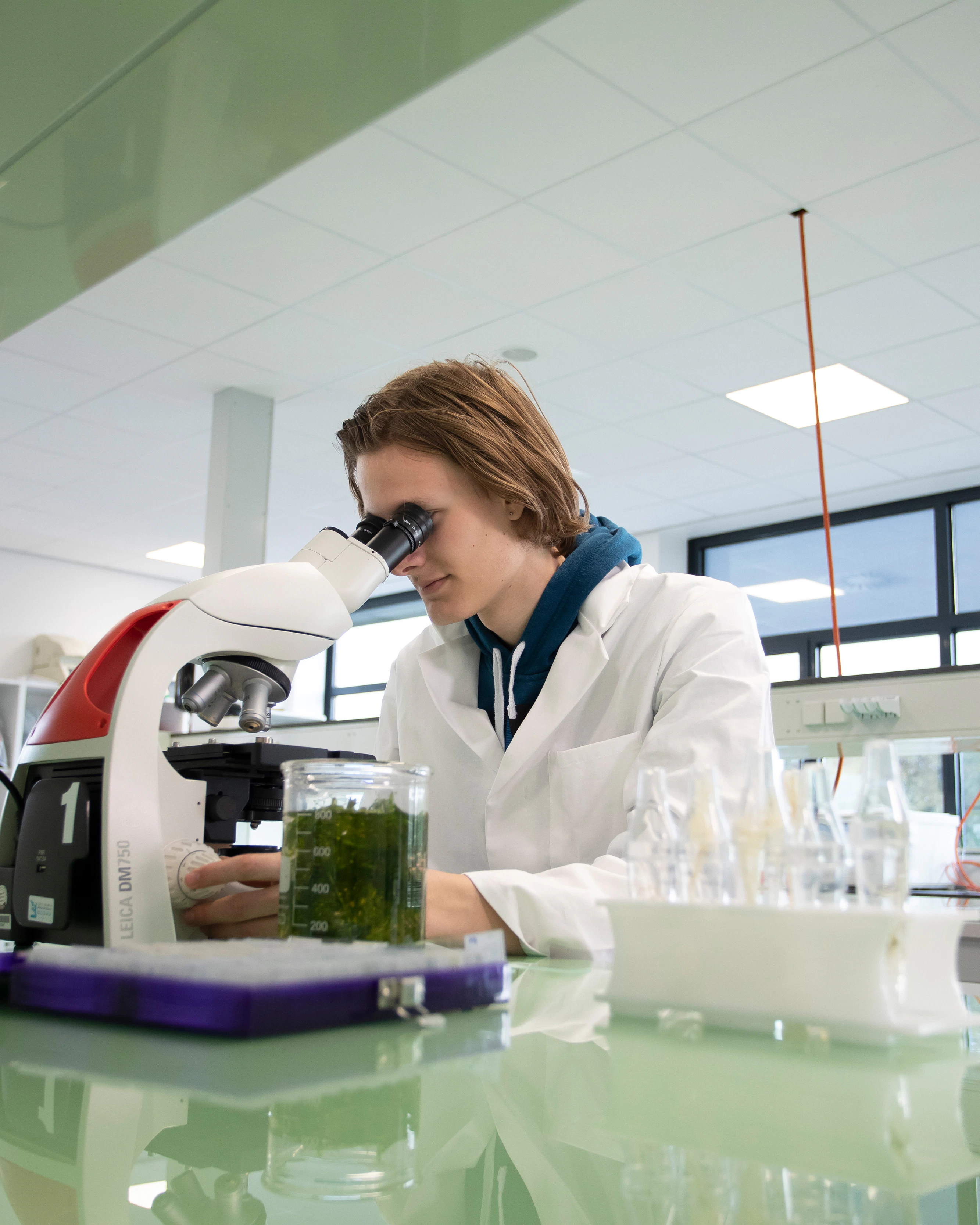 Jongen in een labaratoriumjas zit achter een microscoop