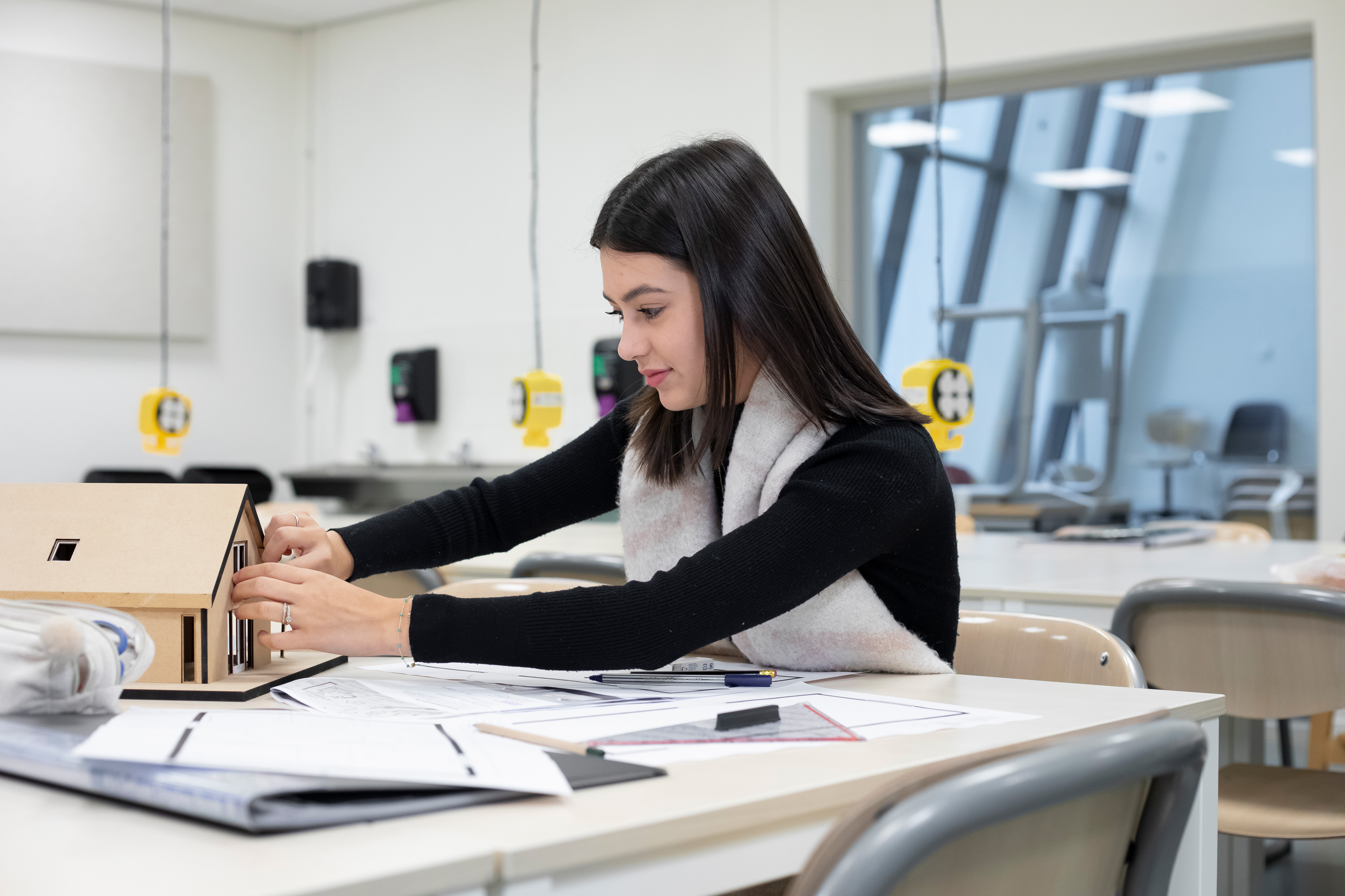 Meisje is bezig met een maquette terwijl op de tafel pennen en papier liggen