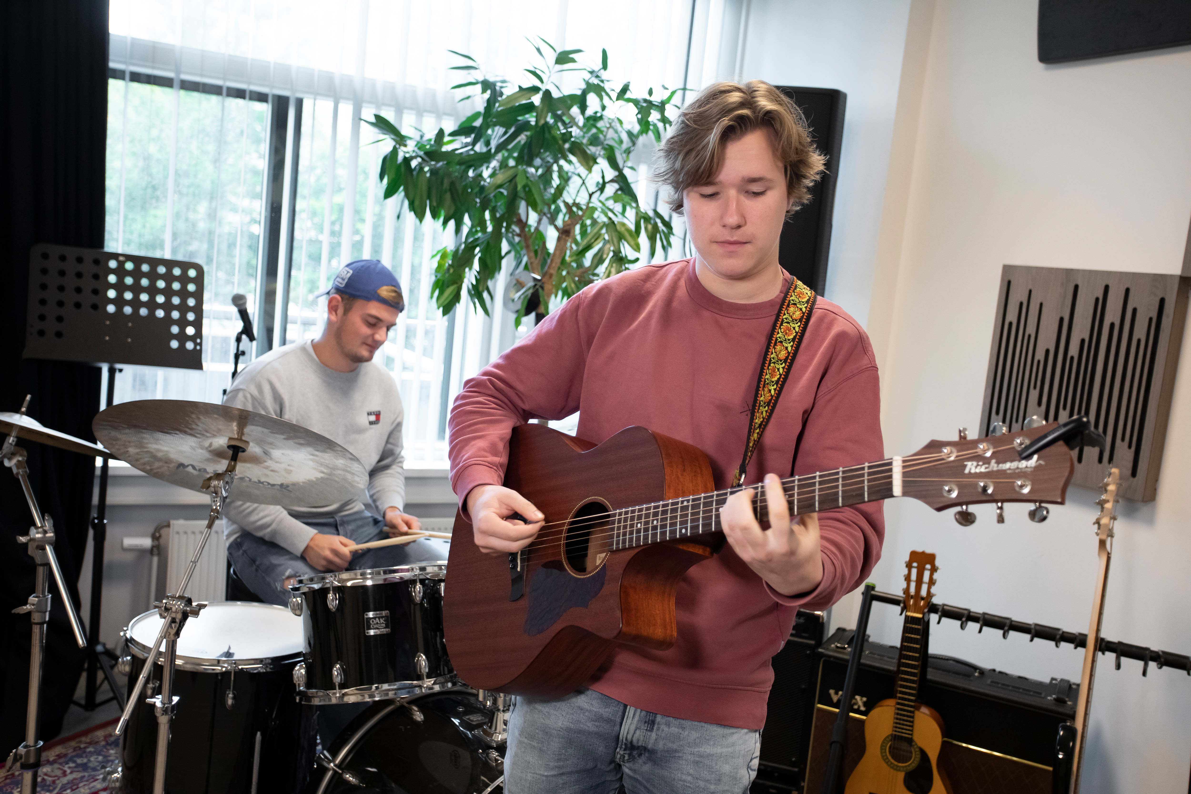 Een jongen speelt gitaar en de andere jongen is aan het drummen