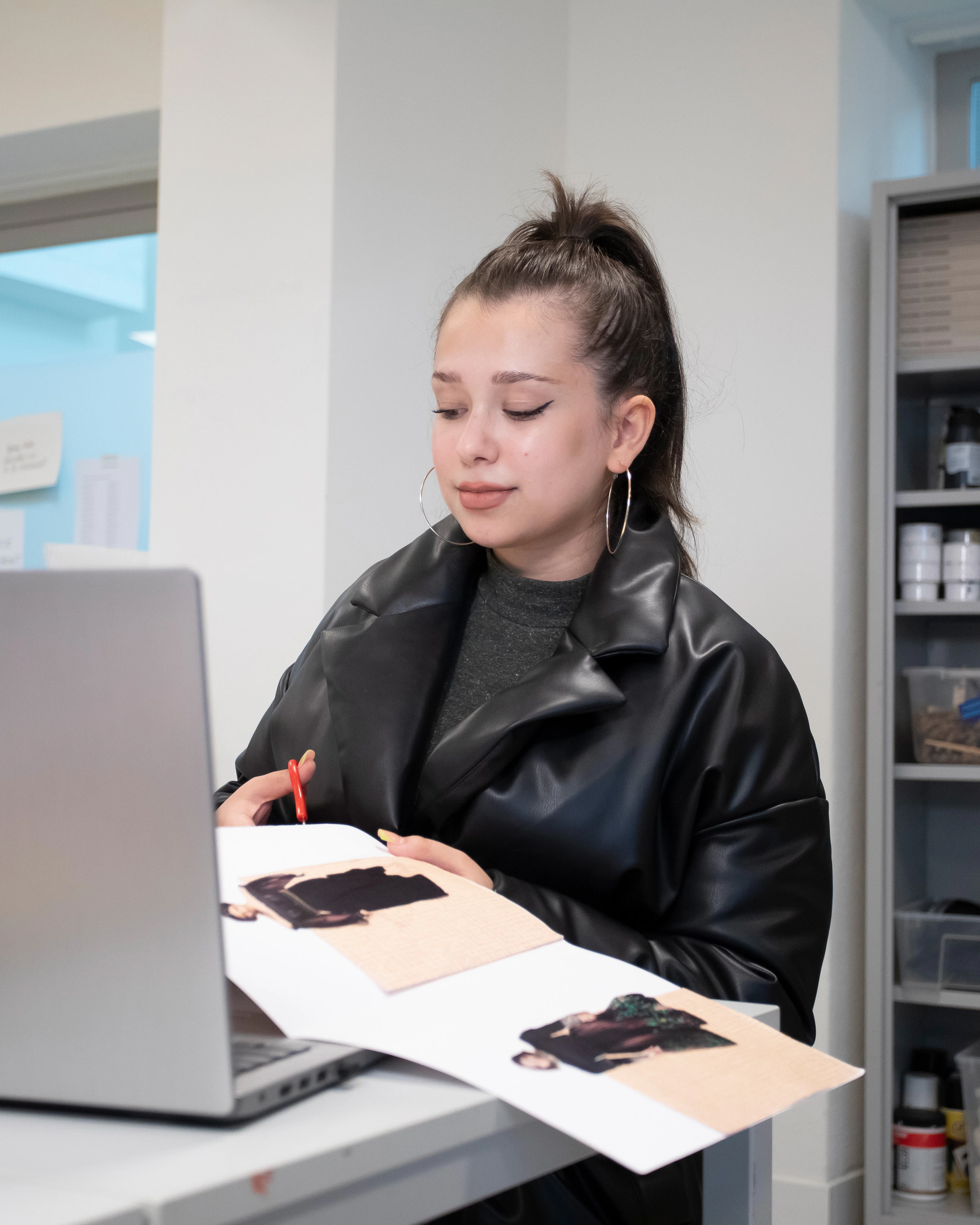 Student zit achter een laptop en knipt iets uit een boek