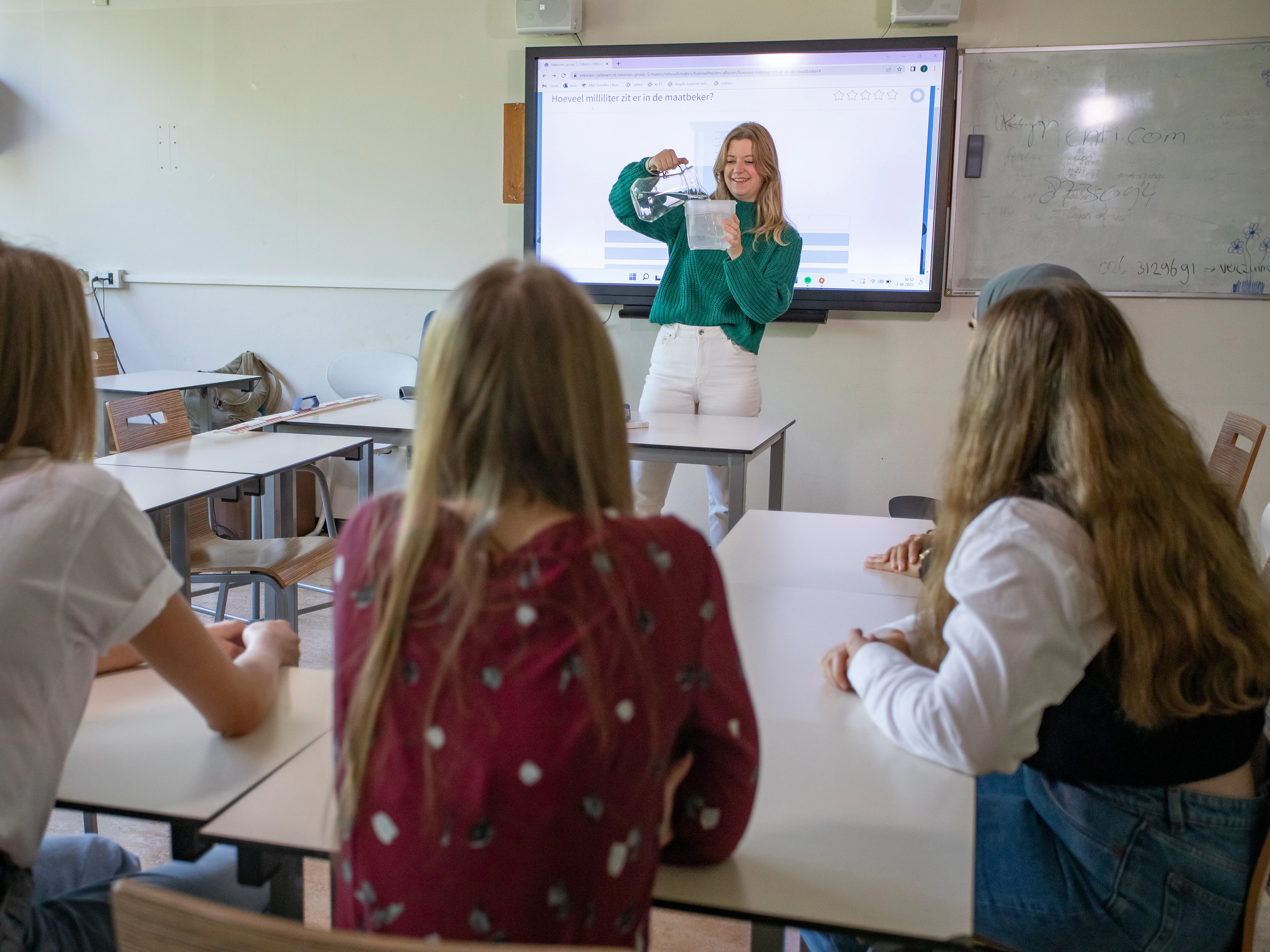 Student staat voor de klas met een maatbeker
