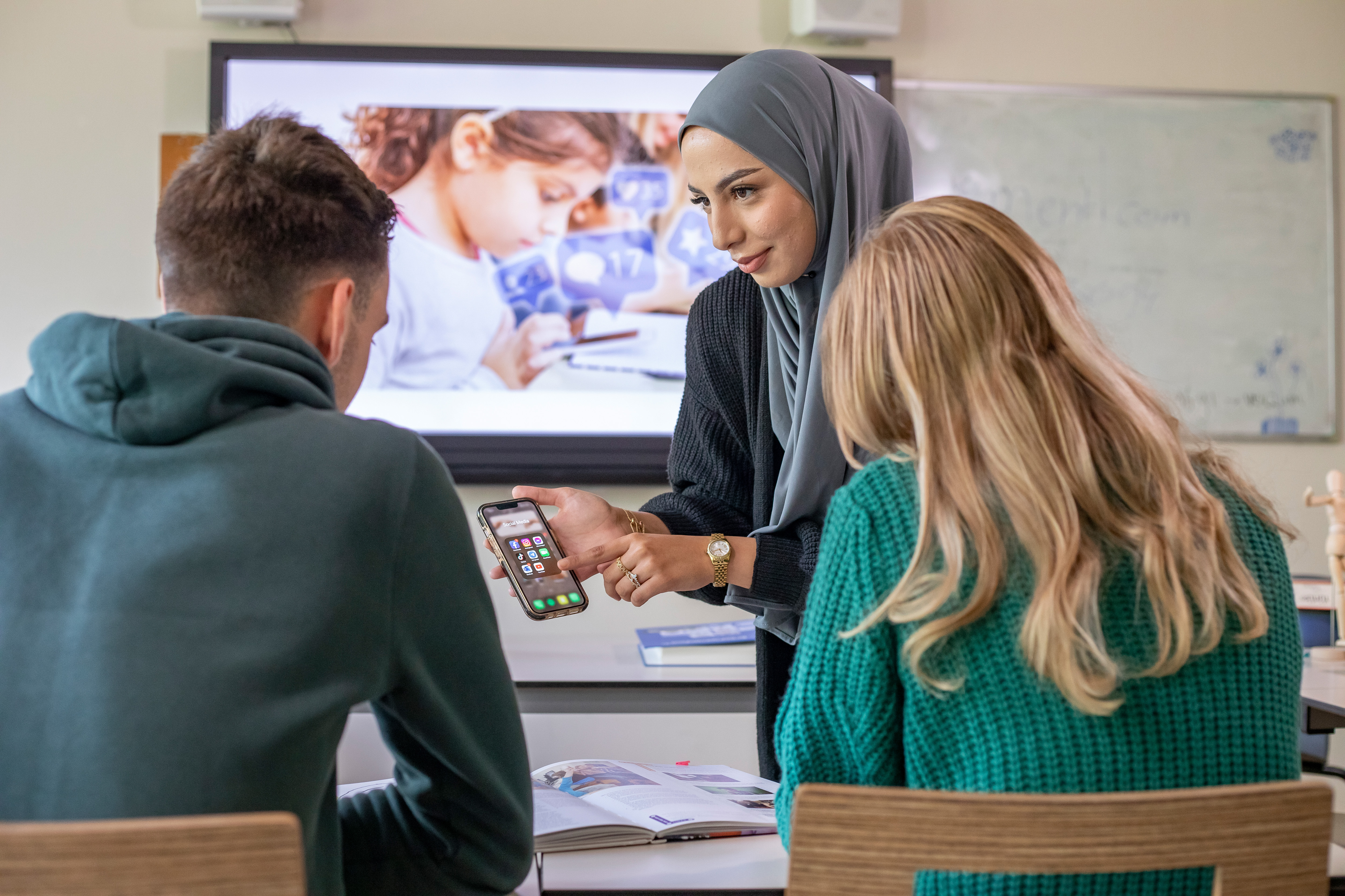 Student wijst op een telefoon en staat voor 2 studenten