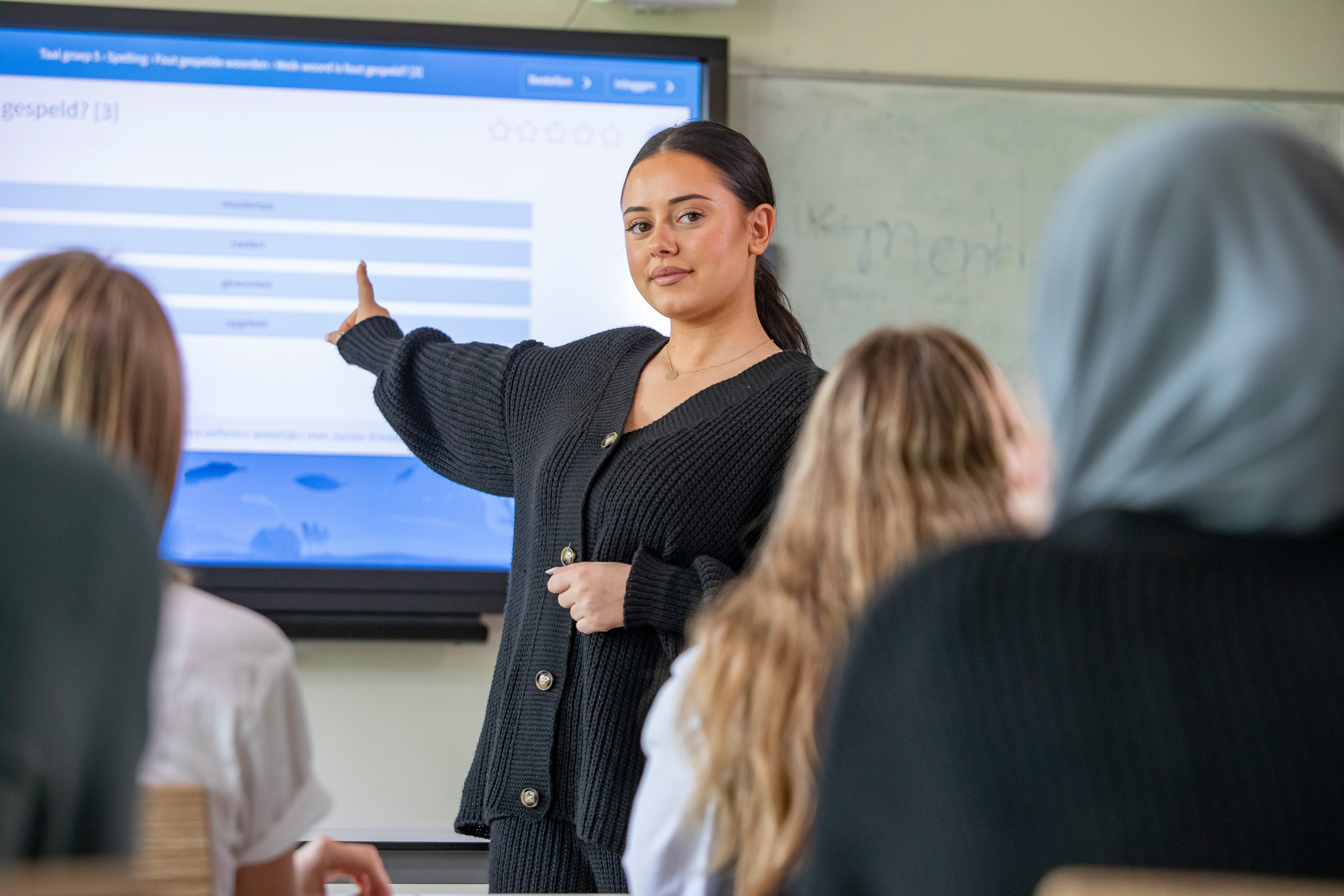 Student staat voor de klas en wijst naar het bord
