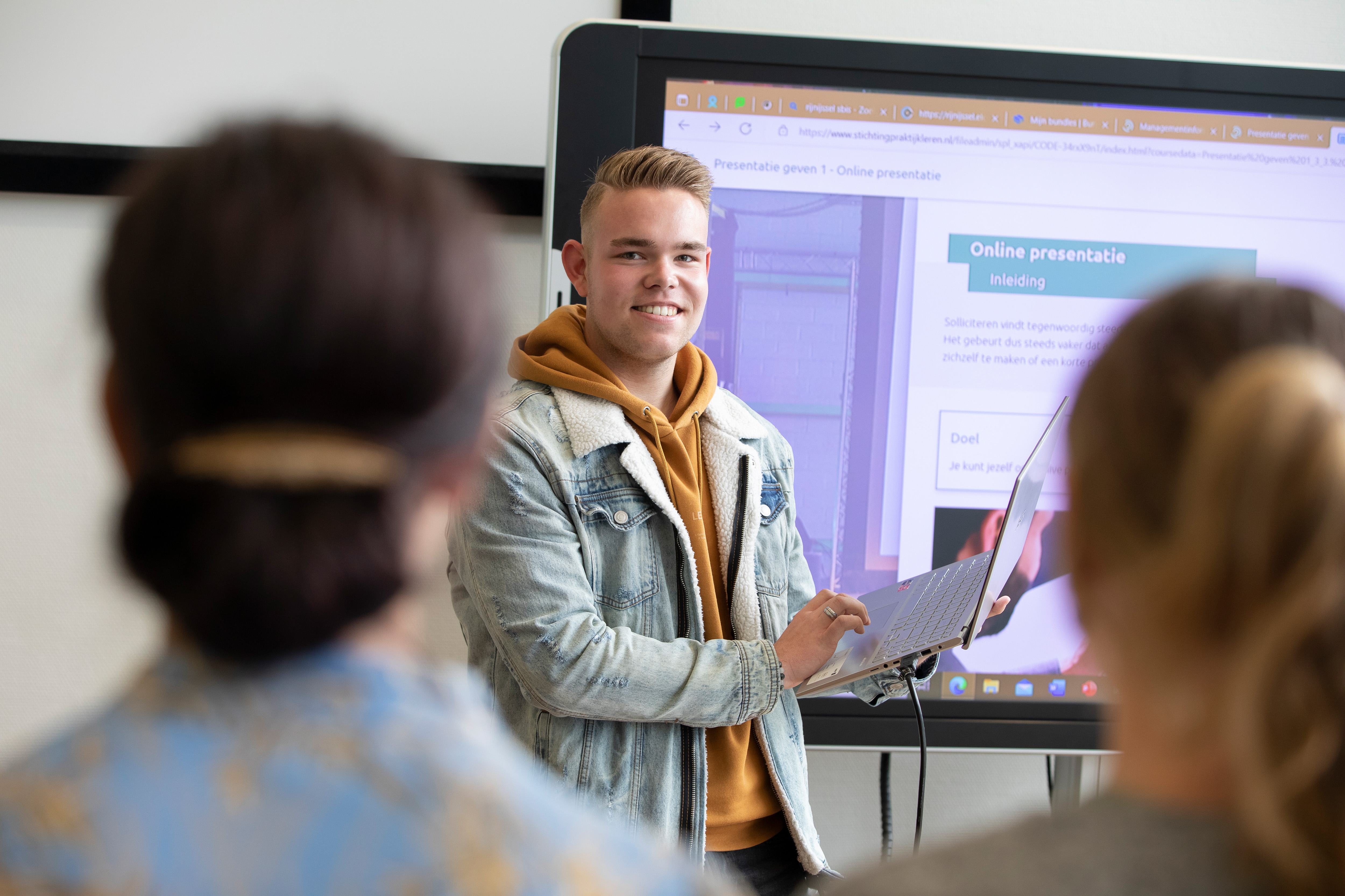 Student staat voor de klas en heeft een laptop in zijn hand