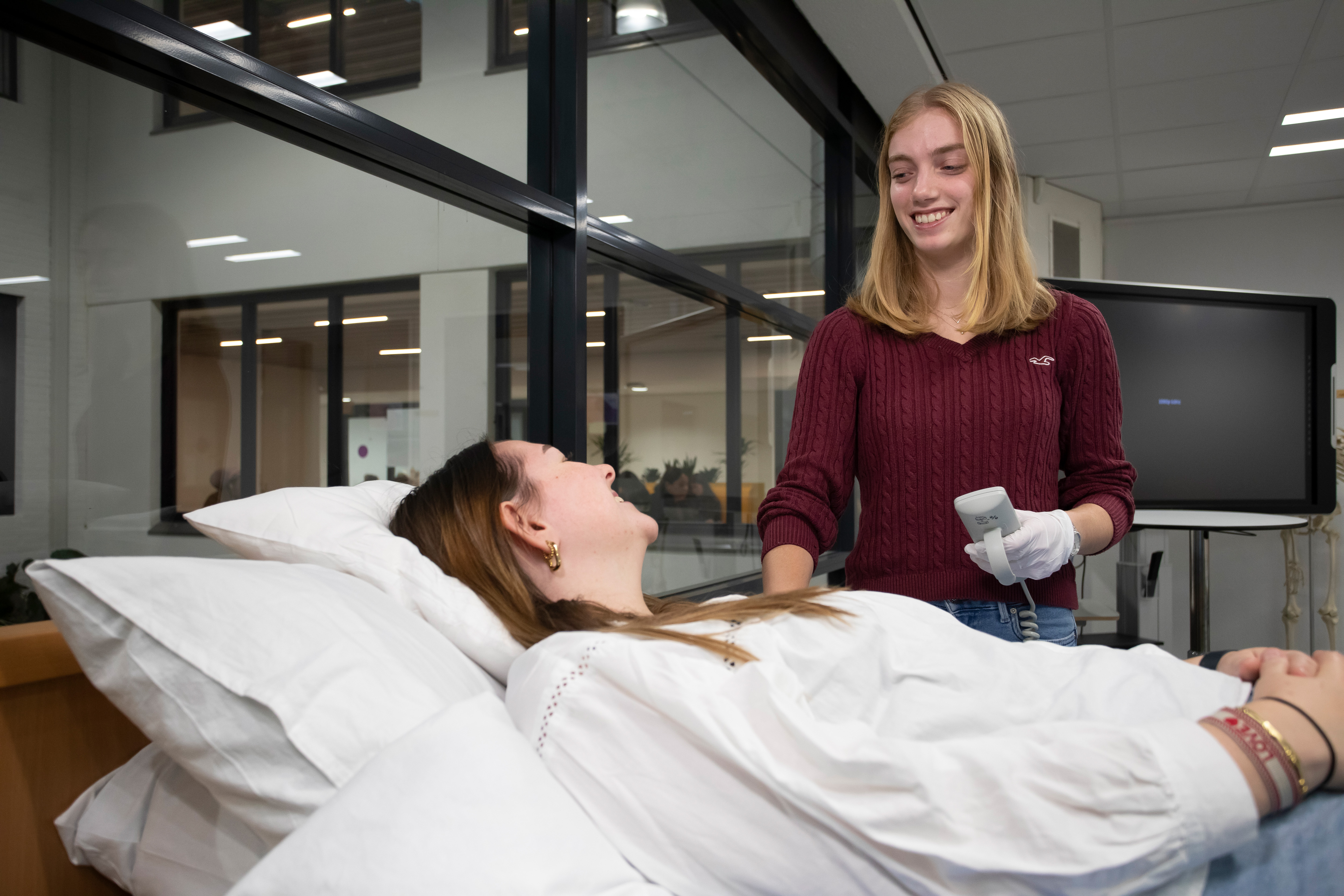 Student staat langs een bed waar iemand op ligt en heeft een afstandsbediening in de hand