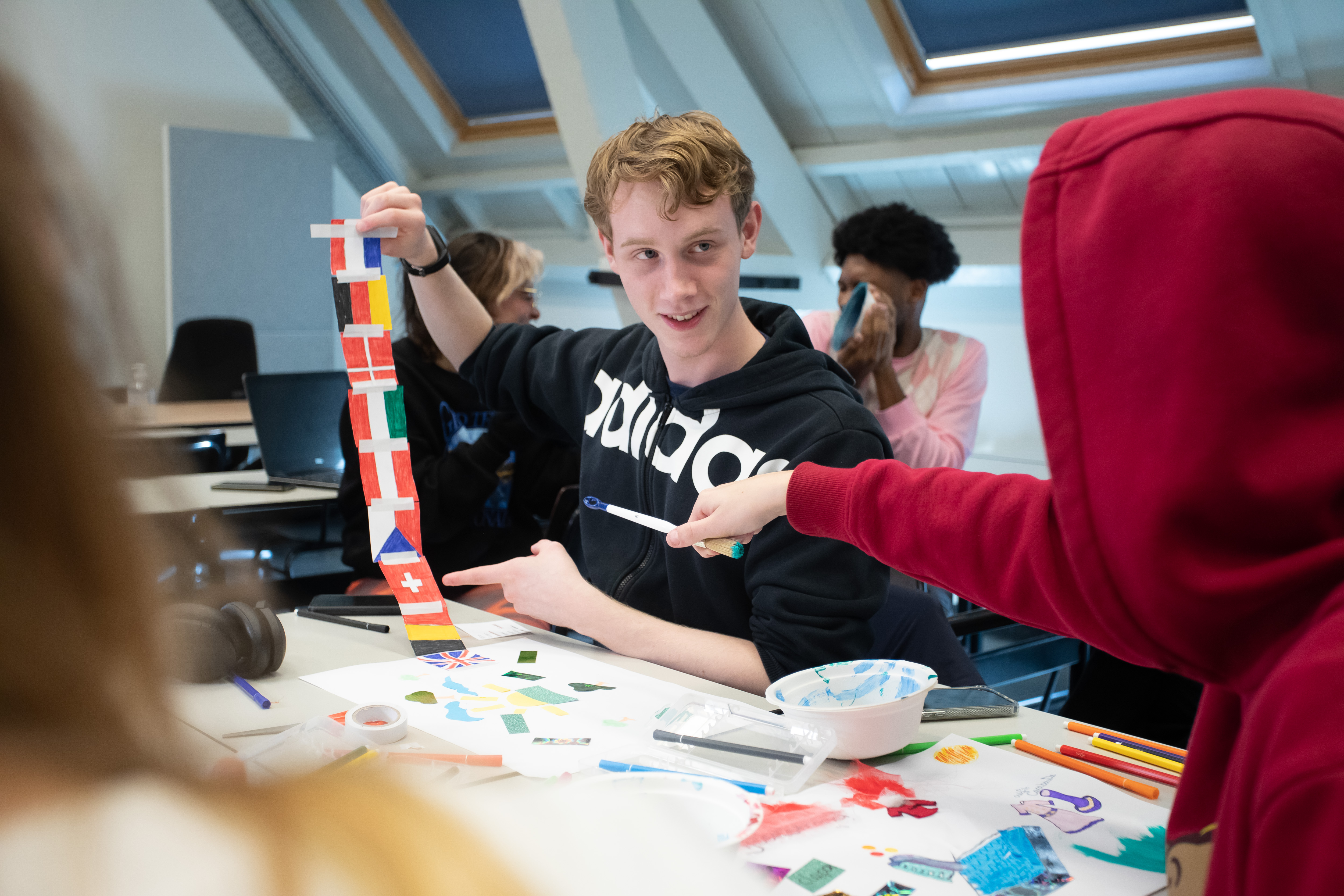 Student wijst naar een andere student die een aantal vlaggen van landen in zijn hand houdt
