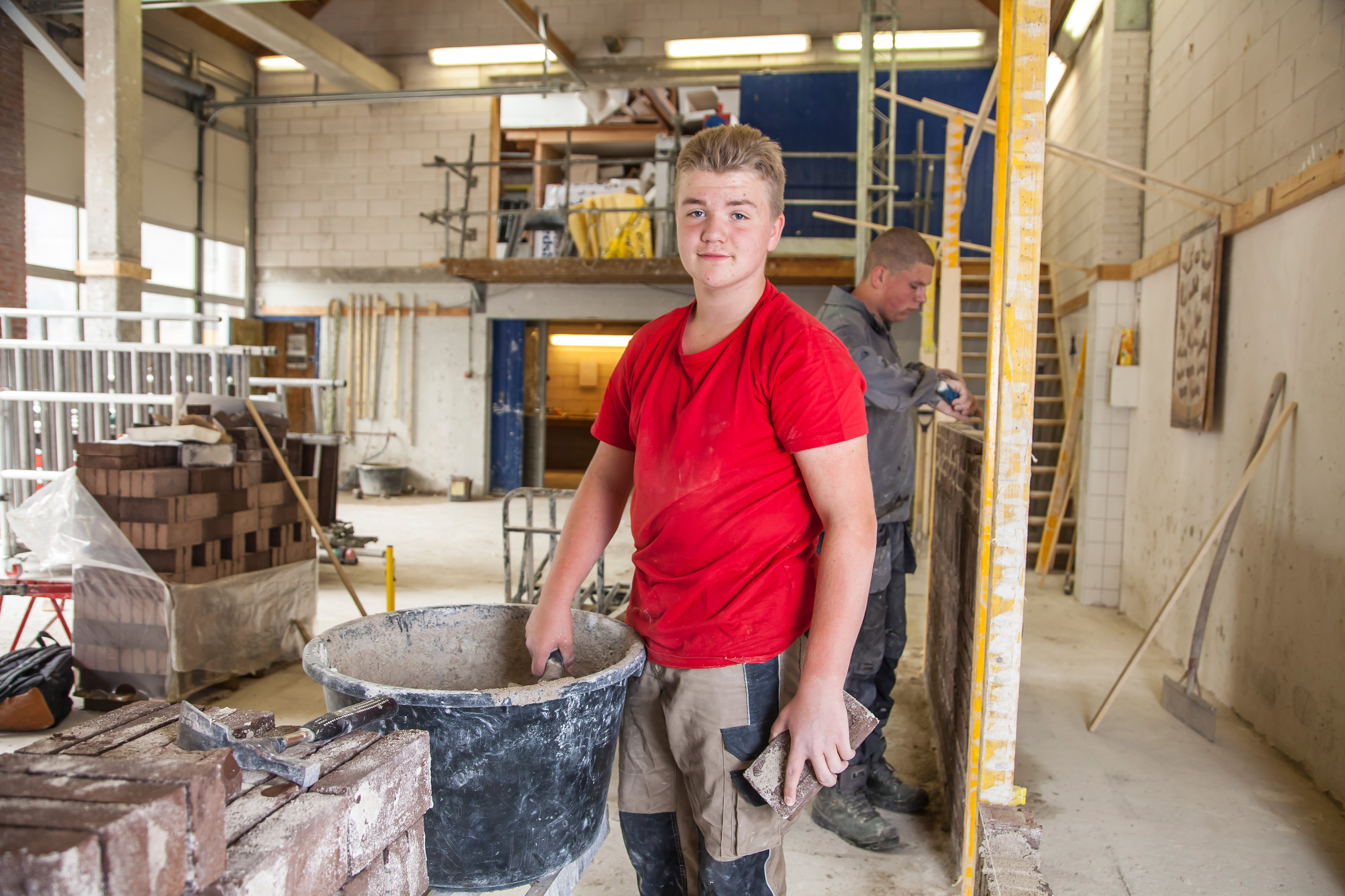 Jongen staat naast emmer met cement en kijkt naar camera
