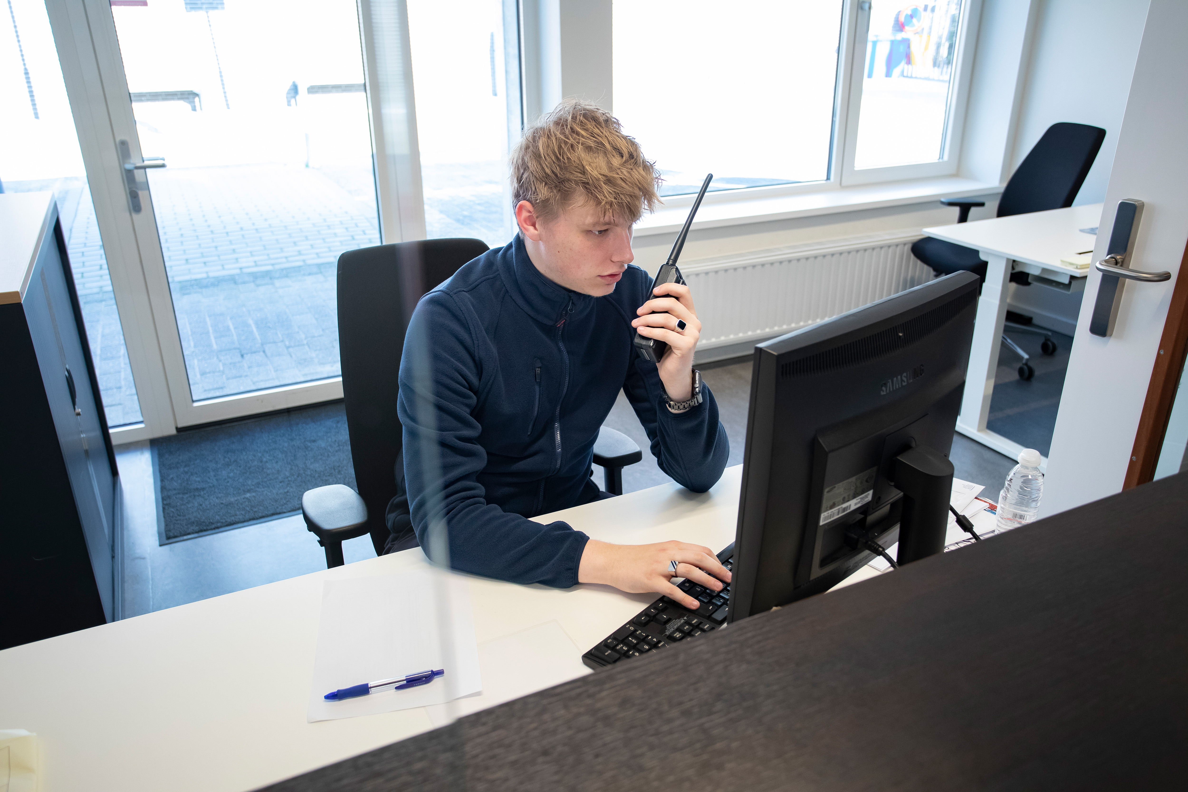 Student zit achter een computer en heeft een portofoon vast