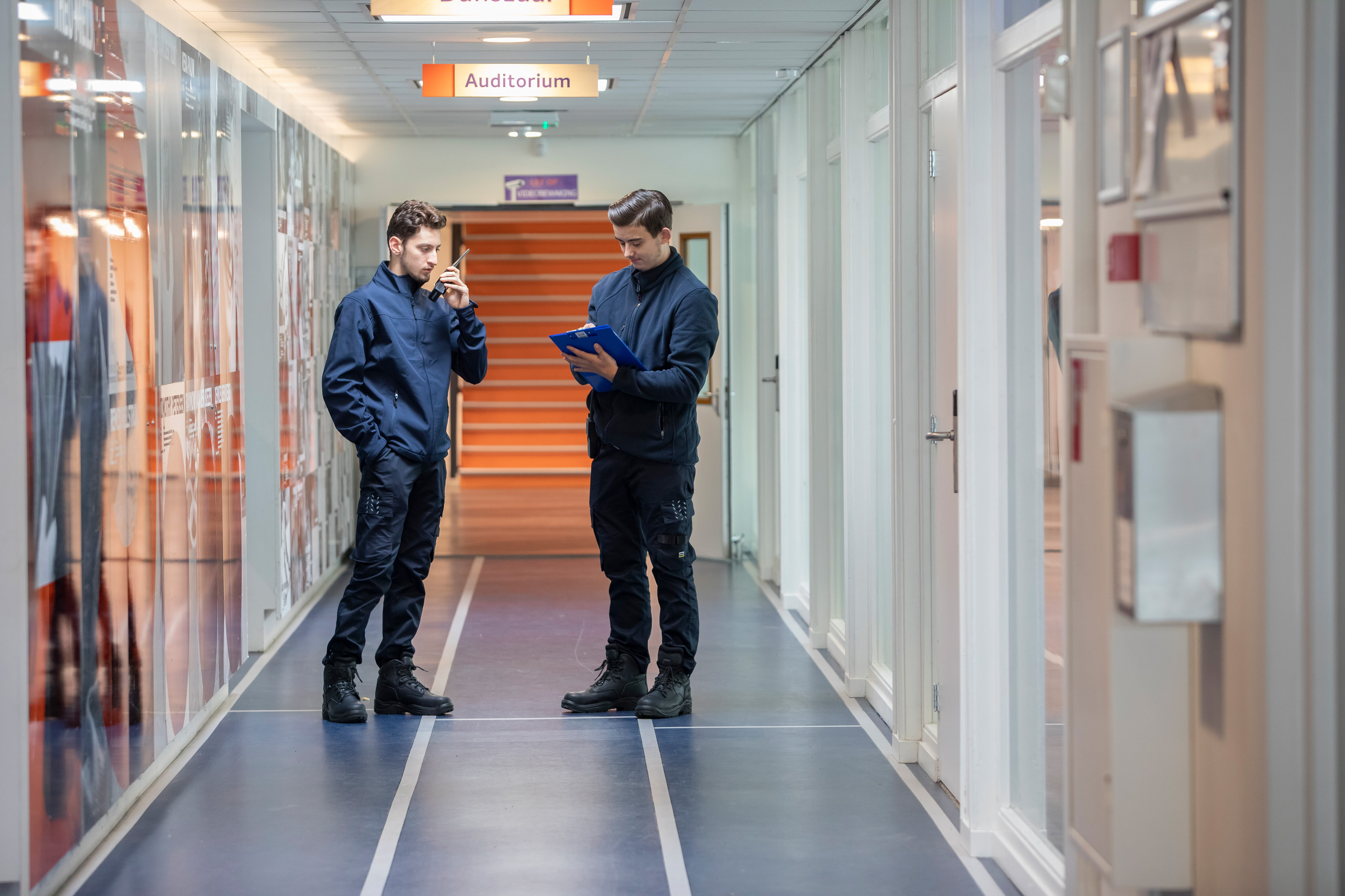 Studenten staan in de gang. Een student houdt een portofoon vast terwijl de ander iets opschrijft